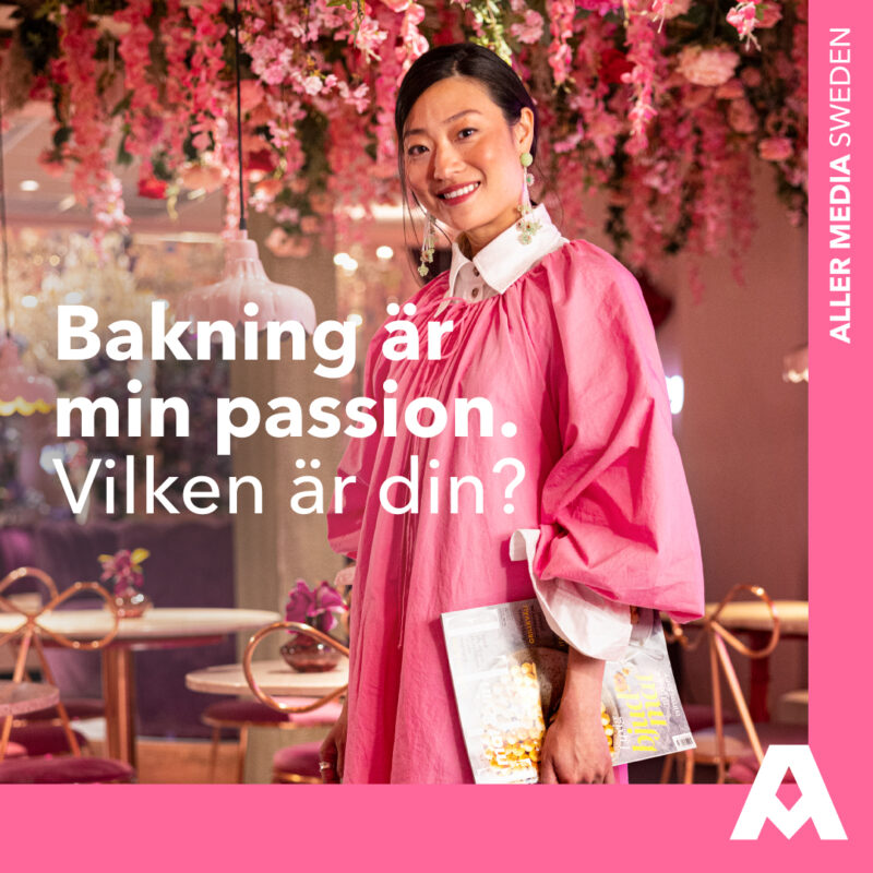 En kvinna en rosa klänning som ler medan hon håller i en tidning om Bakning från Aller Media